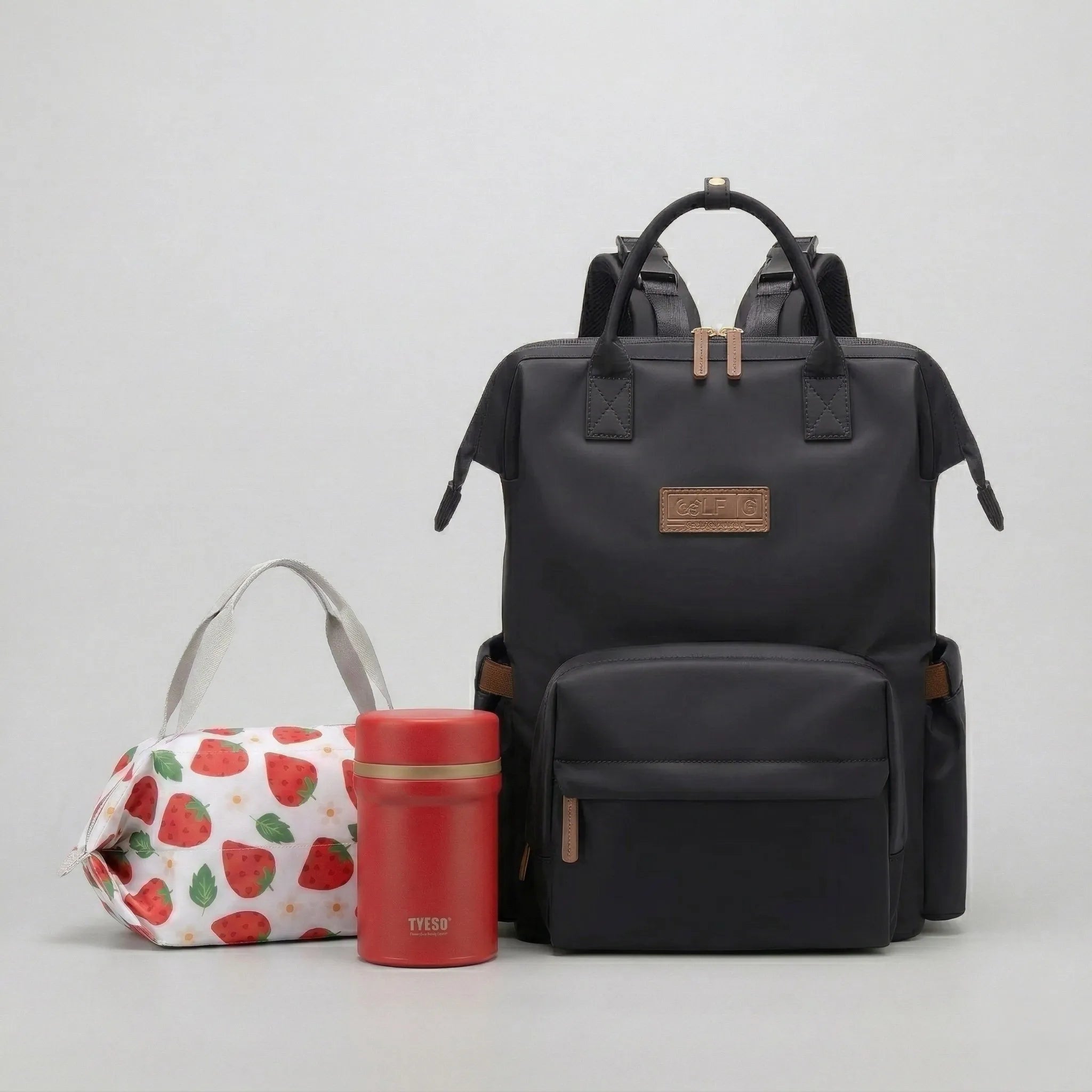 Ensemble complet Le Goodn'Family comprenant le sac à dos à langer Nyla noir multipoches, le lunch bag isotherme FreshBox motif fraise et la lunch box FreshMeal rouge.