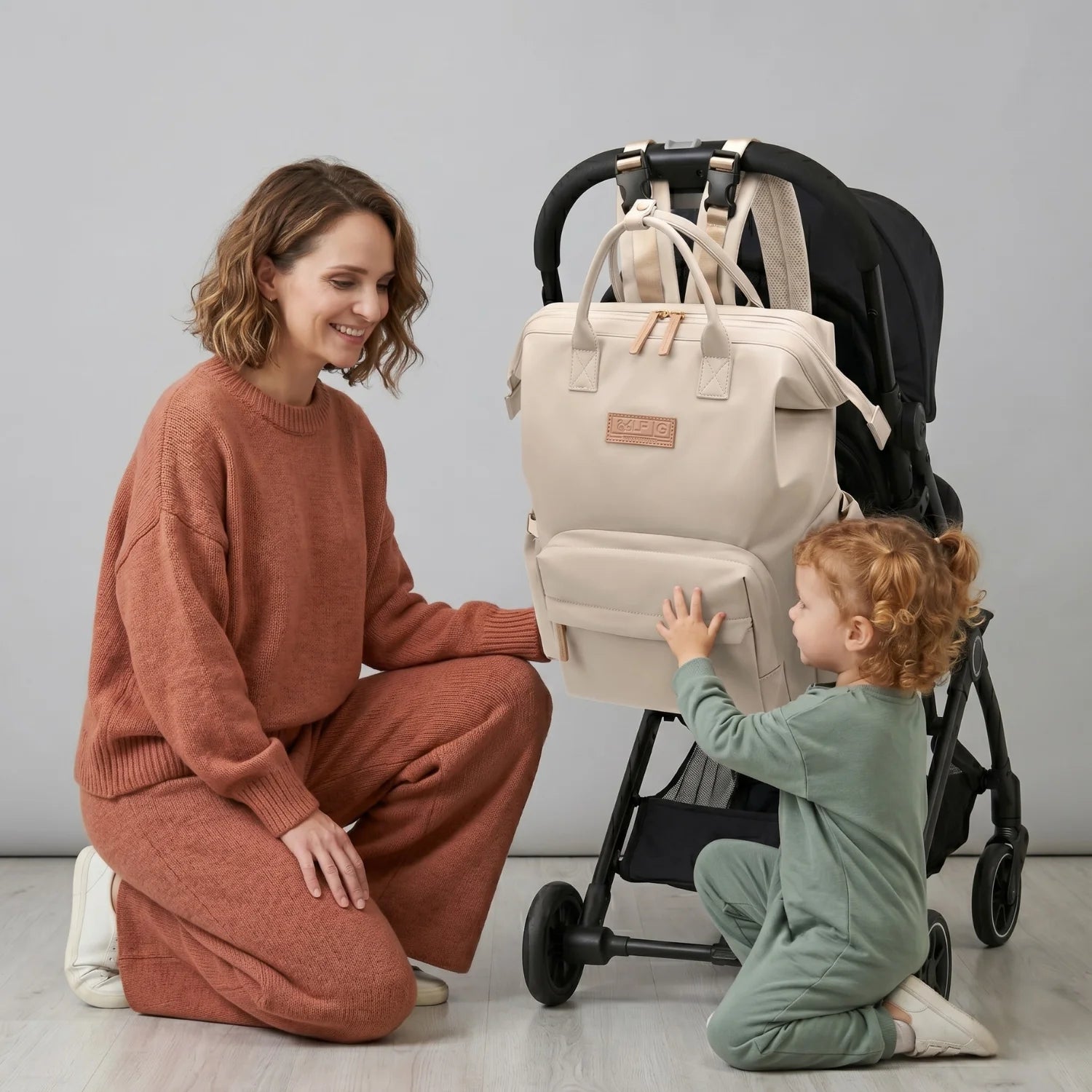 Mère et sa famille profitant d'une sortie avec la poussette équipée du sac à langer élégant Nyla beige déperlant. Avec son design ingénieux pour biberons et lingettes, ce sac Oxford de 760g est parfait pour une organisation sans compromis de style pour les familles actives.