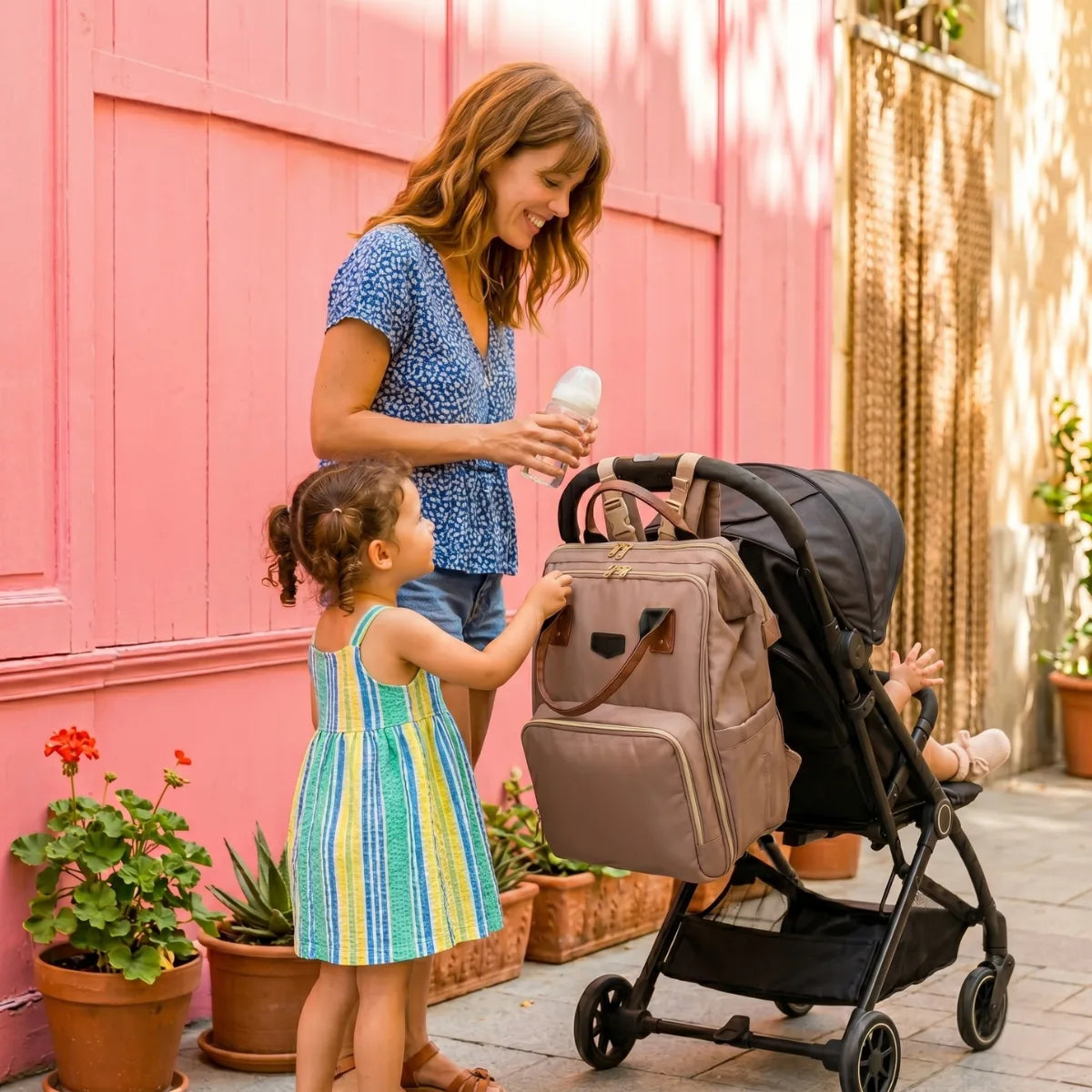 Maman et sa petite fille en balade avec une poussette équipée d'un grand sac à dos à langer moka. Un modèle pratique illustrant le guide du meilleur sac à langer en 2026.