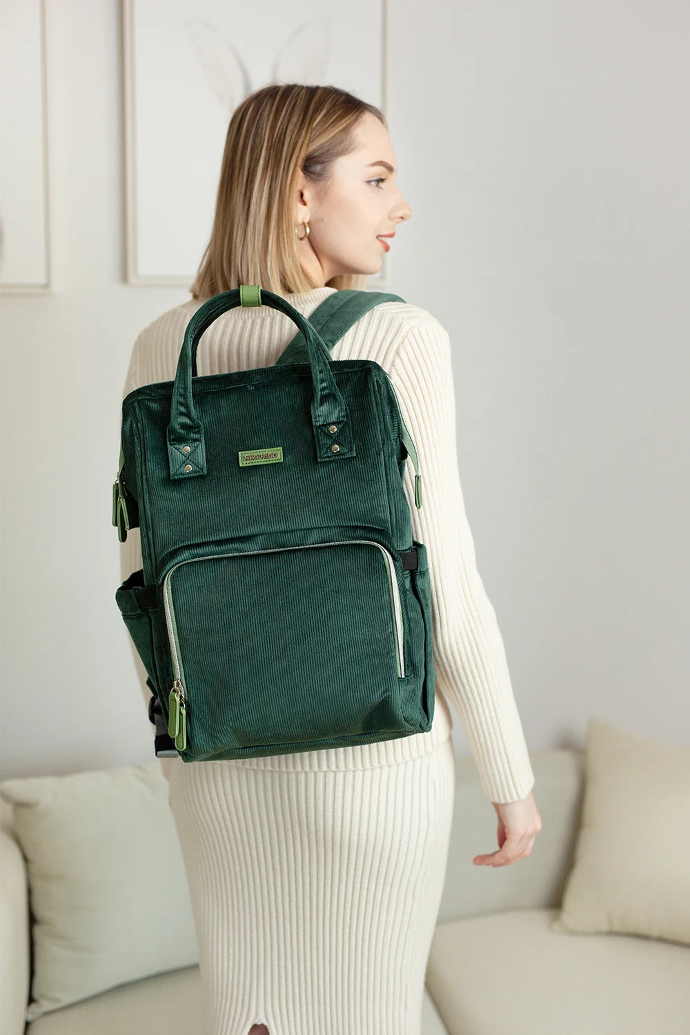 Maman portant un sac à langer en tissu premium, élégant et pratique, avec plusieurs rangements pour bébé.

