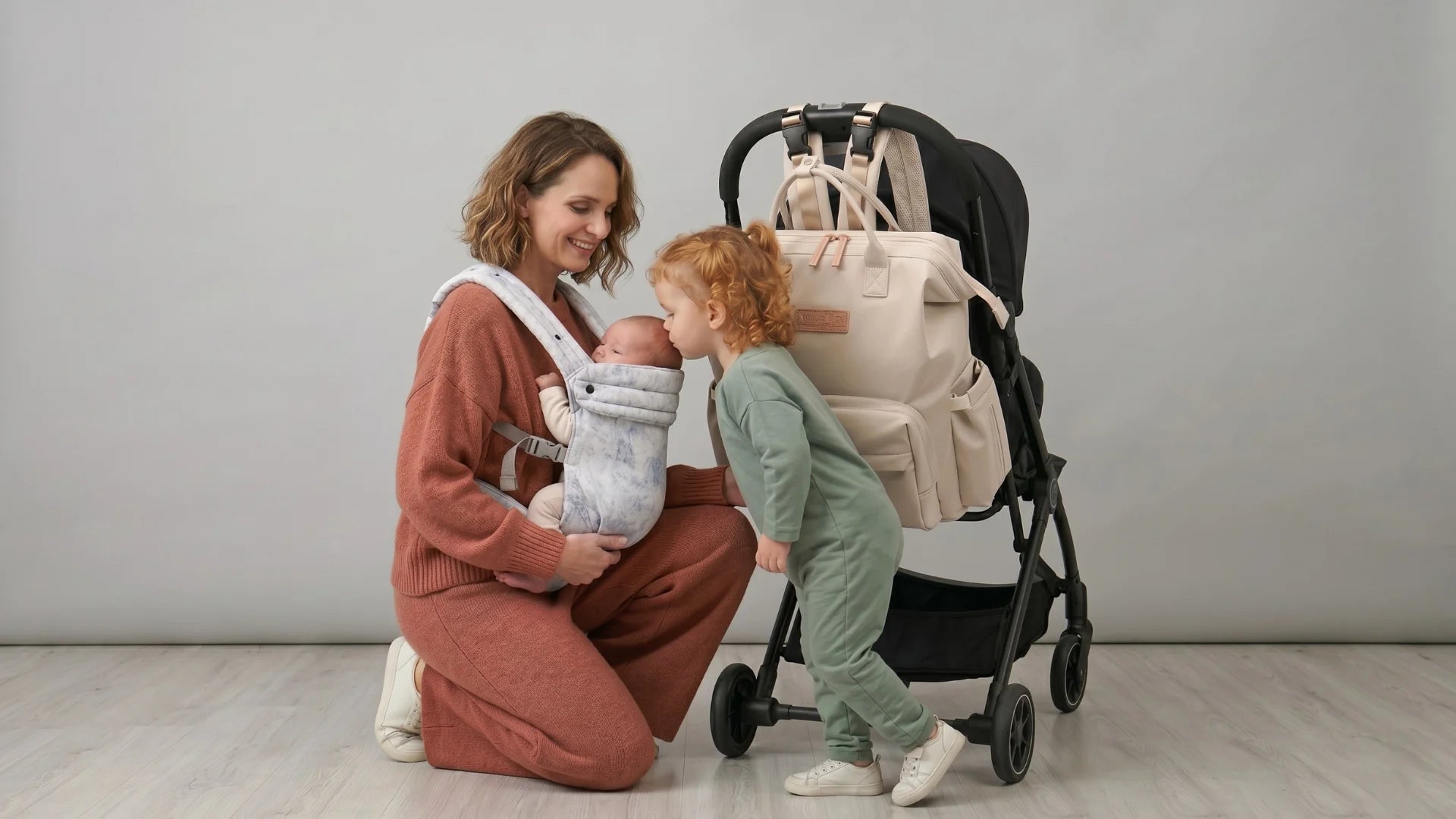 Maman utilisant un porte-bébé physiologique avec sa fille, illustrant la collection premium de packs maternité, sacs à langer et accessoires pour parents nomades