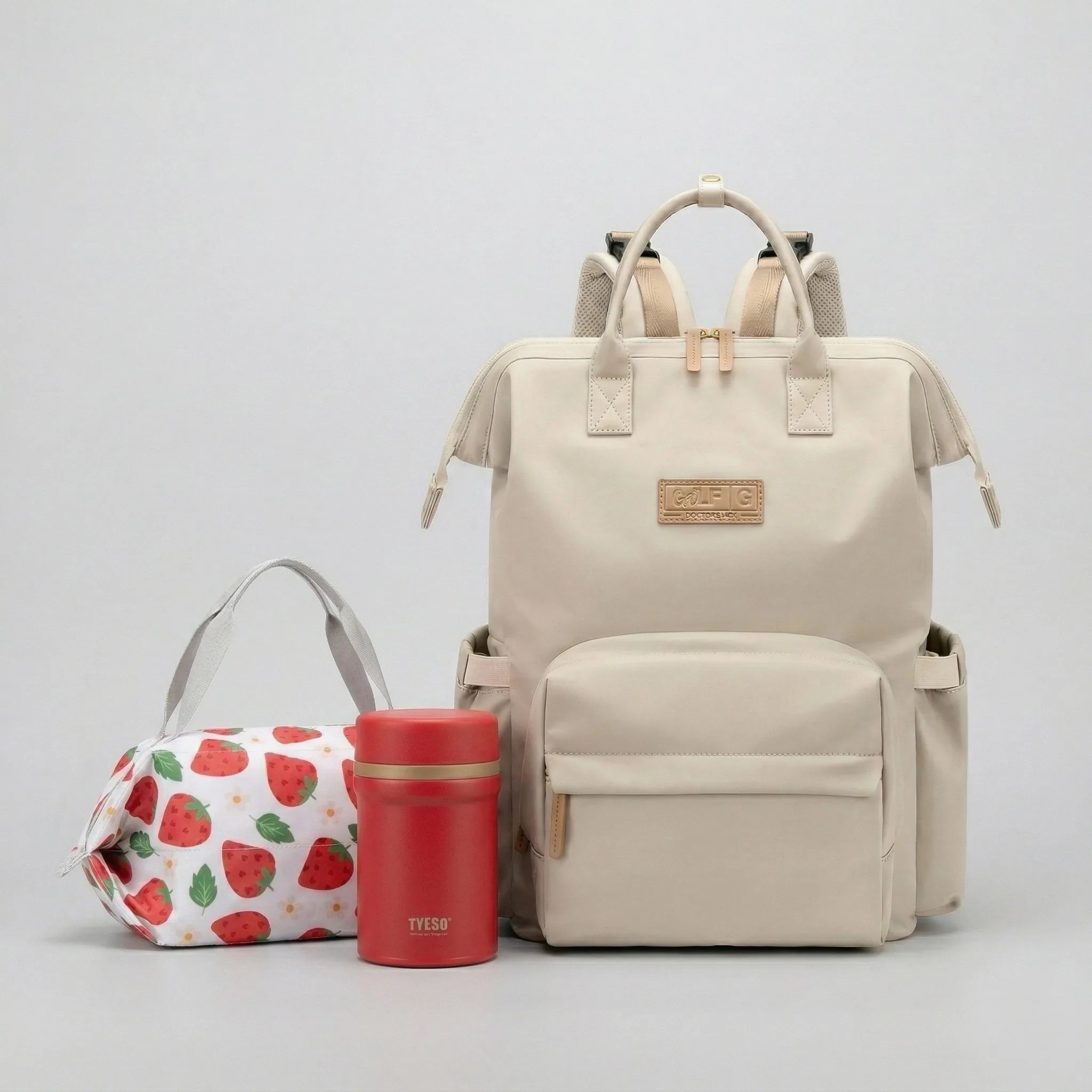 Kit de maternité et voyage avec le sac à langer dos Nyla beige, accompagné du sac repas isotherme FreshBox fraise et de la bento box inox rouge.