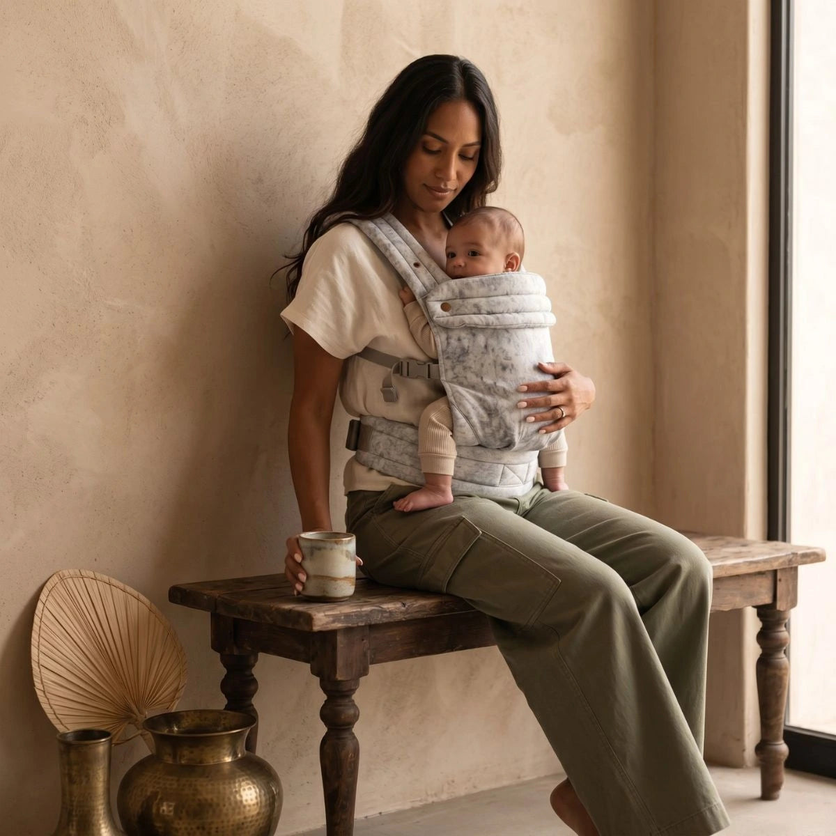 Porte-bébé ergonomique et physiologique HarmoBaby en coton et lin respirant, maman assise en intérieur avec son bébé installé en position physiologique de portage.