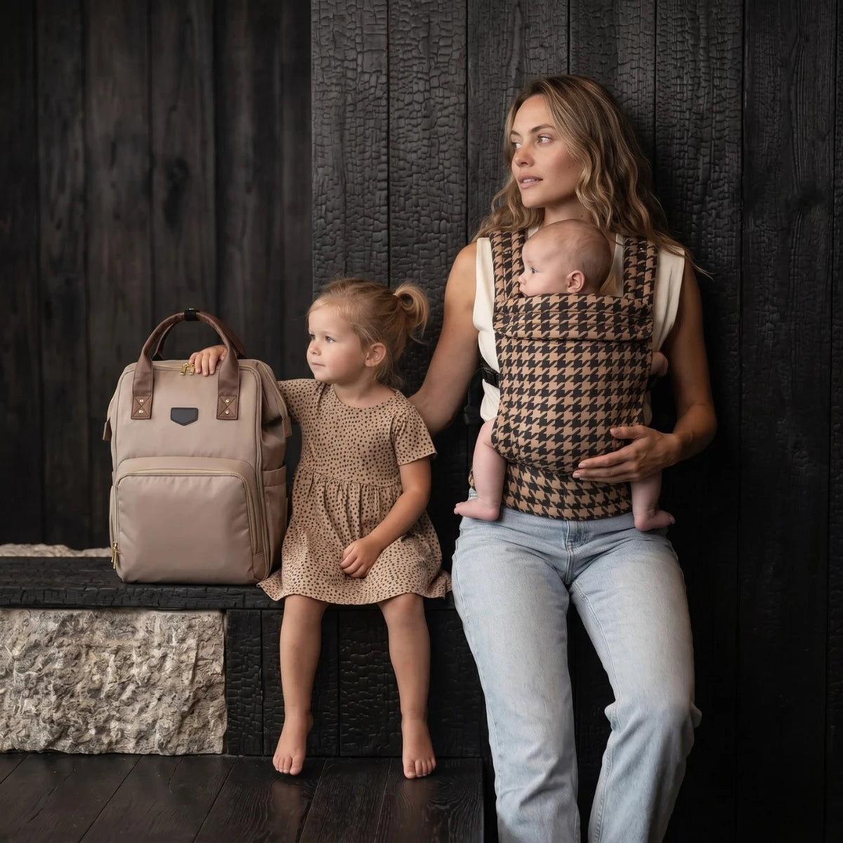 Maman utilisant le porte bébé ergonomique HarmoBaby au motif pied de poule avec son nourrisson aux côtés de sa fille et du sac à dos à langer Moka marron beige posé dans une rue urbaine chic Goodnvibes