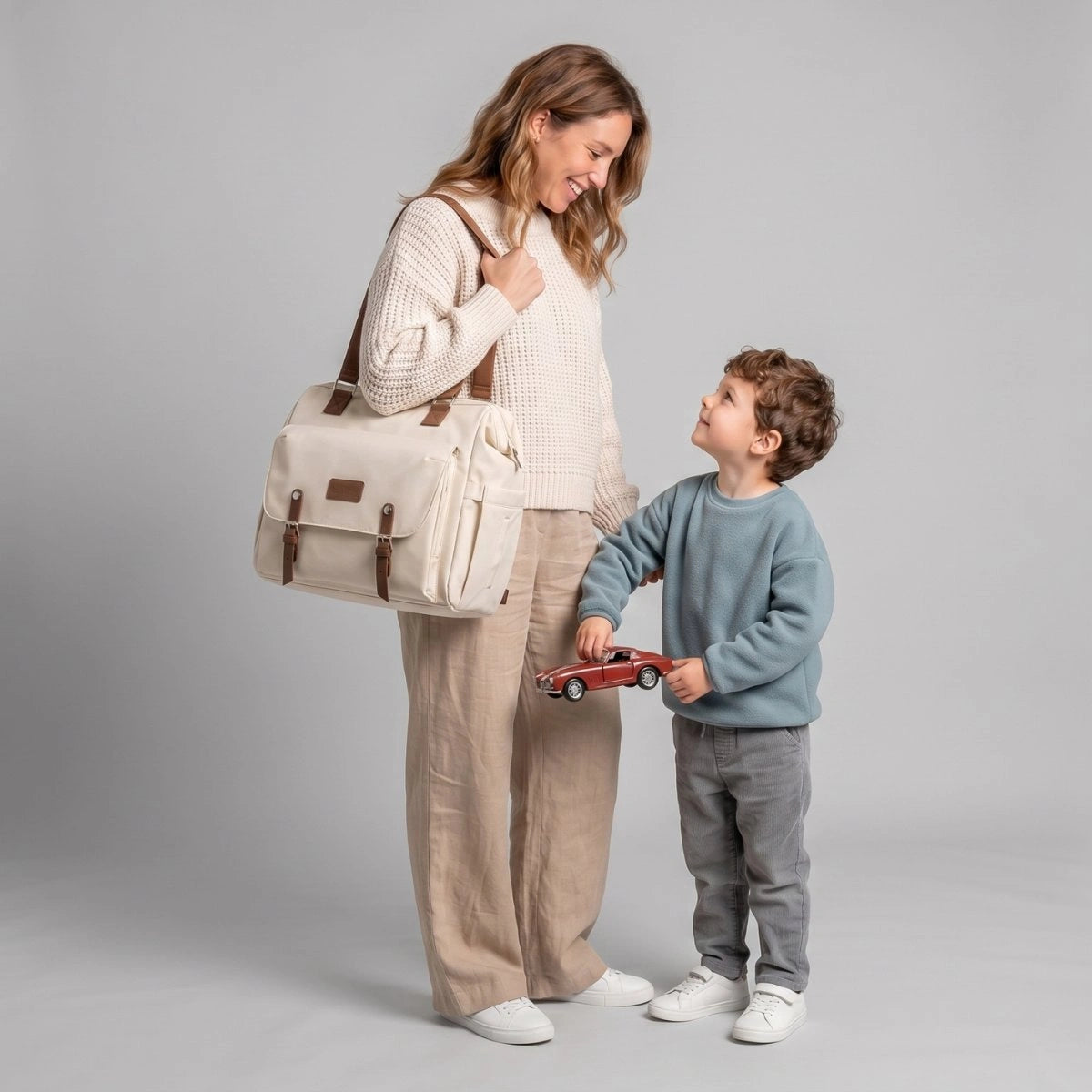 Maman portant le sac à langer Aventure beige élégant à l'épaule avec son petit garçon.