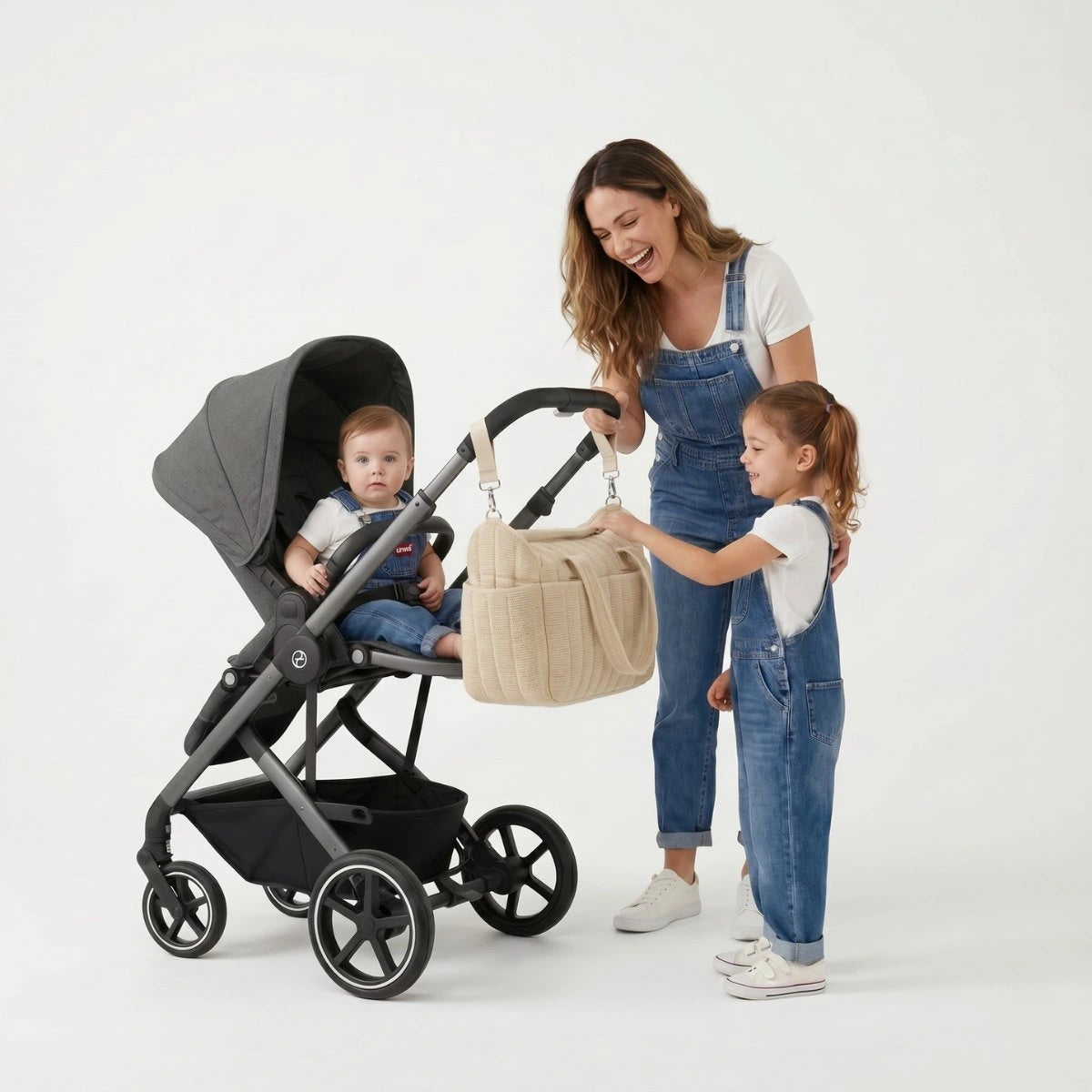 Maman souriante installant le sac à langer souple CozyTote sur le guidon de sa poussette à côté de sa grande fille.