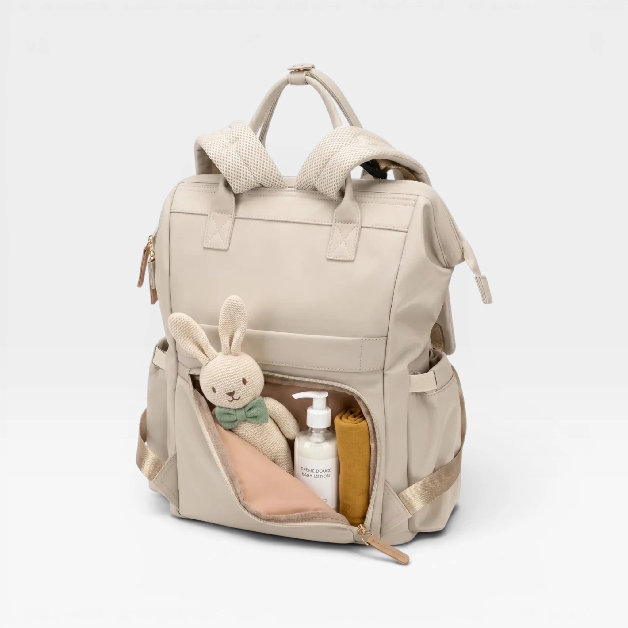 Sac à langer Nyla beige contenant les essentiels de bébé : couches, produits de soin et doudou.